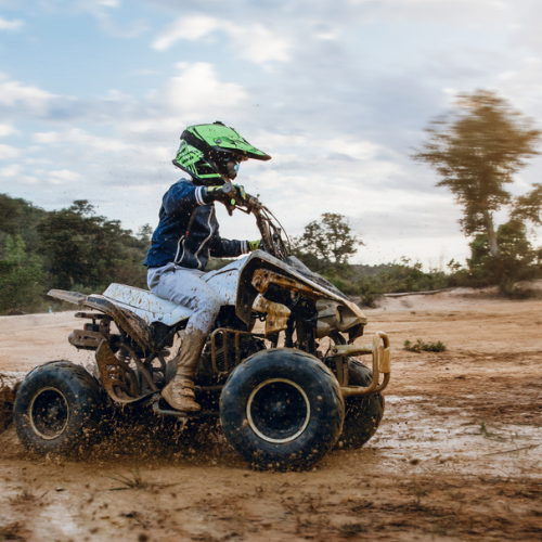 Child on a 110cc quad bike, riding in the mud, wearing a helmet